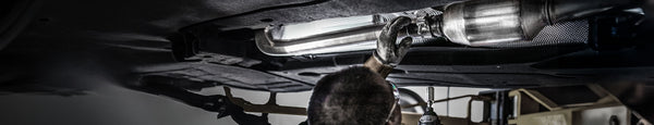 Under-car view of an automotive technician installing an EPA-Compliant MagnaFlow Direct-Fit Catalytic Converter on, featuring OEM-grade fit and bolt-on installation.